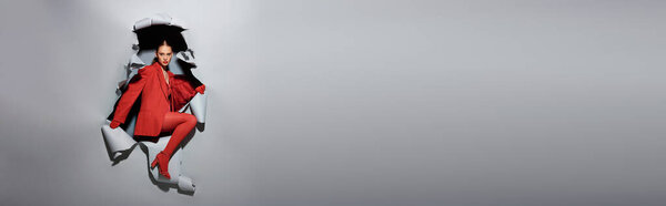 знамя молодой женщины в красном наряде с смелым макияжем, прорывающимся через рваный серый фон с отверстием