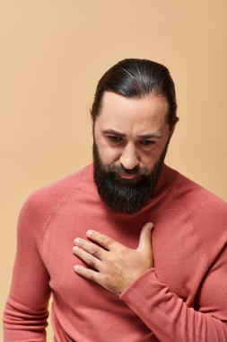 portrait of serious and handsome man with beard in pink turtleneck jumper on beige background clipart