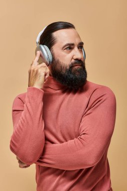 Balıkçı yaka kazaklı yakışıklı adam bej arka planda kablosuz kulaklıkla müzik dinliyor.