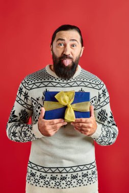 Kış süveteri içinde, Noel hediyesini tutan ve dili kırmızıya yapışan komik sakallı adam.