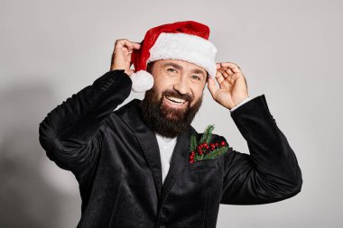 Gri arka planda Noel Baba şapkası takan zarif takım elbiseli yakışıklı bir adamın portresi.