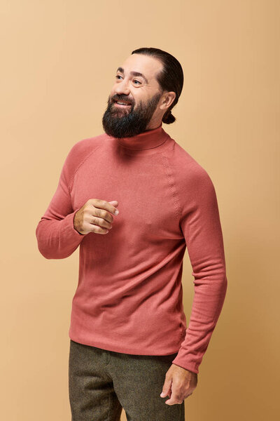 happy man with beard in pink turtleneck jumper smiling cheerfully on beige backdrop
