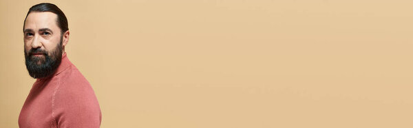 portrait, handsome serious man with beard posing in pink turtleneck jumper on beige backdrop, banner