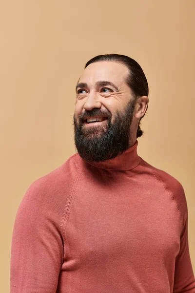 stock image happy man with beard in pink turtleneck jumper smiling cheerfully on beige backdrop