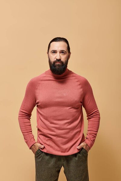 portrait, handsome focused man with beard posing in pink turtleneck jumper  on beige background