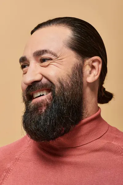 stock image positive man with beard in pink turtleneck jumper smiling cheerfully on beige backdrop