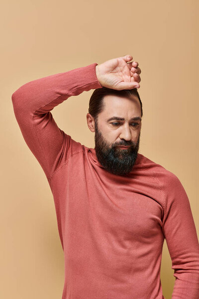 portrait, handsome man with beard posing in pink turtleneck jumper on beige background, serious face