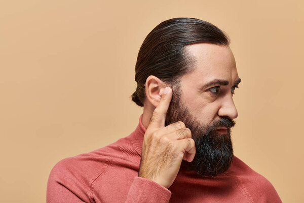 portrait of handsome man with beard posing in turtleneck jumper on beige background, serious