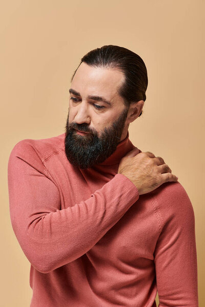 portrait, serious good looking man with beard posing in pink turtleneck jumper on beige background