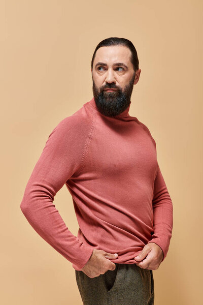 portrait, serious and handsome man with beard posing in pink turtleneck jumper  on beige background