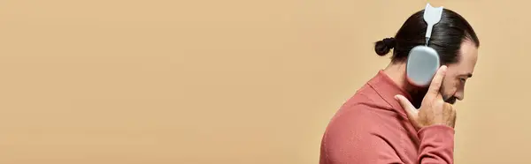 サイドビューバナー ベージュのワイヤレスヘッドフォンで音楽を聞くタートルネックジャンパーのひげ付き男 — ストック写真
