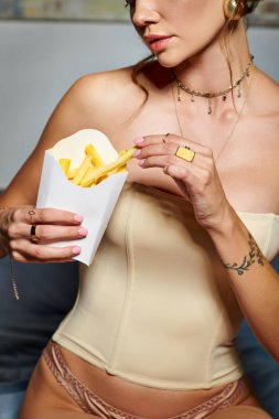 Bej korseli, elinde patates kızartması ve aksesuarlarla poz veren genç seksi bir kadın.