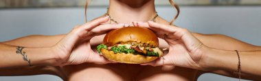 Aksesuarlı ve elinde kocaman bir hamburger dövmesi olan genç bir kadının kırpılmış görüntüsü.