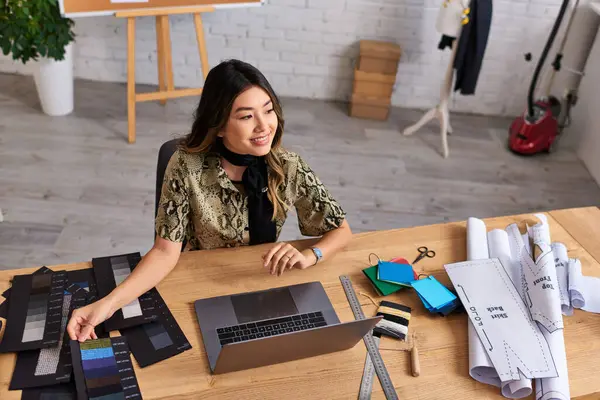 stock image happy asian fashion stylist smiling near laptop and color swatches with sewing patterns in atelier