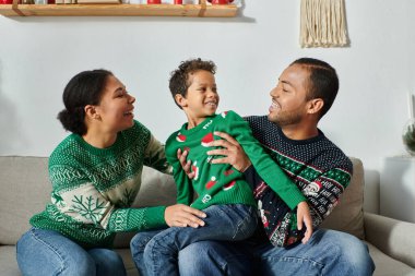 cheerful african american parents with their kid sitting on lap wearing warm Christmas sweaters clipart