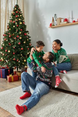 İyi görünümlü Afro-Amerikan ailesinin Noel ağacının yanında mutlu bir şekilde gülümsemesinin dikey görüntüsü.