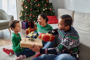 Güzel, neşeli Afro-Amerikan ailesi Noel ağacının yanında hediyelerini takıyor.