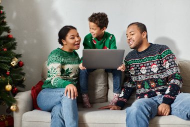 Neşeli Afro-Amerikalı kadın, oğlu ve kocasıyla Noel filmi izlerken şaşırmış görünüyor.