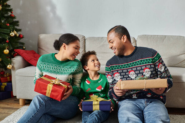 joyous african american parents looking lovingly at their son and holding presents, Christmas