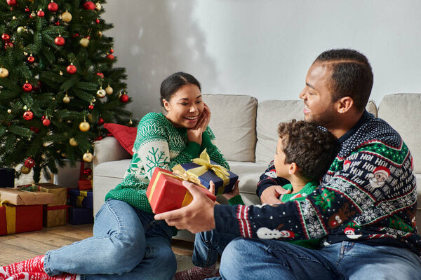 joyous dreamy african american woman looking lovingly at her cheerful son and husband, Christmas