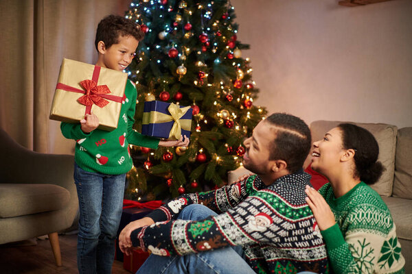 happy african american parents looking lovingly at their cute son holding presents, Christmas