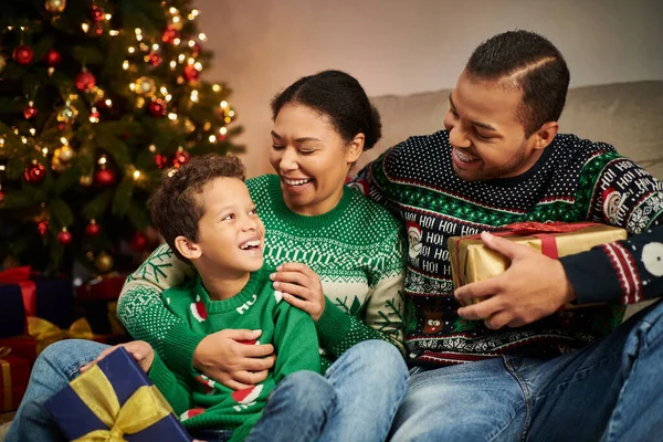 happy african american family sitting next to Christmas tree with garlands and smiling at each other