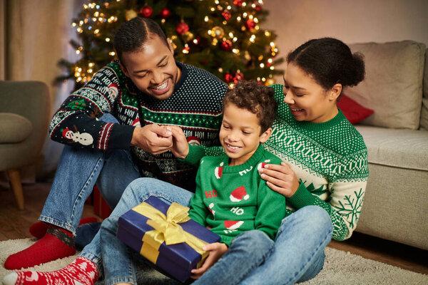 joyous african american parents looking lovingly at their son while he holding Christmas present
