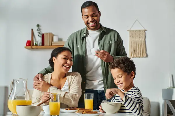 jolly african american parents looking lovingly and smiling at their little son at breakfast table