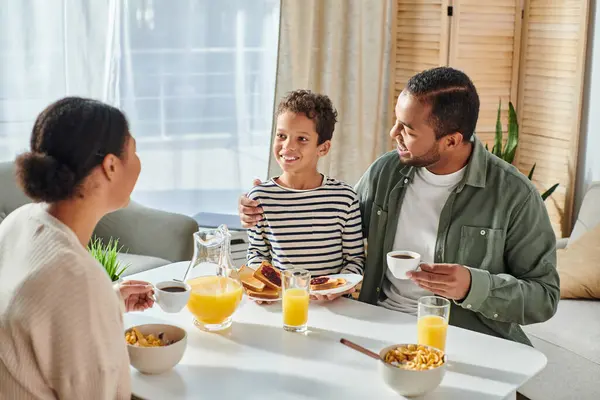 幸せな喜びのアフリカ系アメリカ人の両親は 朝食テーブルで彼らの息子を愛情を持って見ています — ストック写真