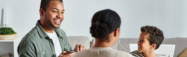 Вид сзади на африканскую женщину, наслаждающуюся завтраком со своим веселым сыном и мужем, баннер