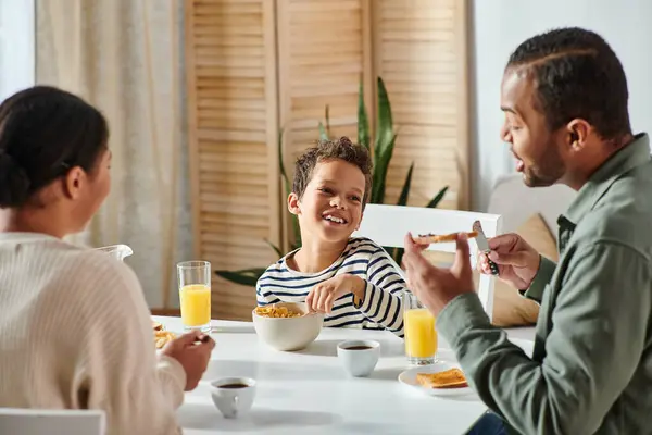 幸せな愛らしいアフリカ系アメリカ人の少年に焦点を当て 朝食テーブルで両親に元気そうに見える — ストック写真