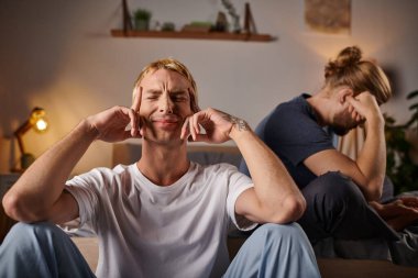 depressed gay man sitting with closed eyes near boyfriend in bedroom at night, troubled relationship clipart