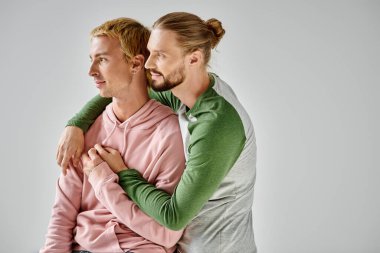 Romantik ve şık eşcinsel çift, gri arka planda dikilirken sarılıp, gözlerini kaçırıyorlar.
