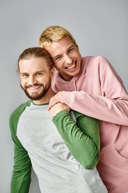 Moda kıyafetleri içinde neşeli eşcinsel çift gri arka plandaki kameraya bakıyor, aşk ve uyum.