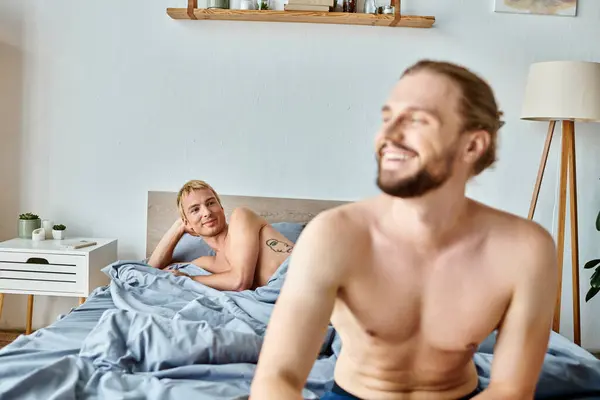 stock image cheerful bearded gay man looking away near love partner lying in bedroom, harmonious relationship