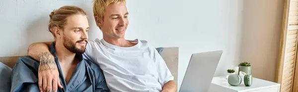 stock image happy tattooed gay man embracing bearded boyfriend while watching film on laptop in bedroom, banner