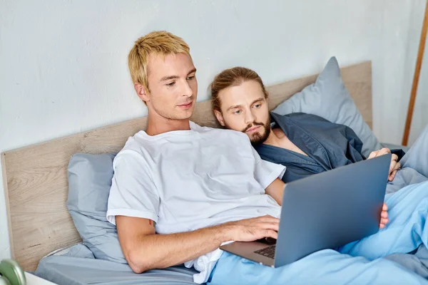 stock image concentrated gay couple watching romantic movie on laptop in bedroom, morning leisure on bed