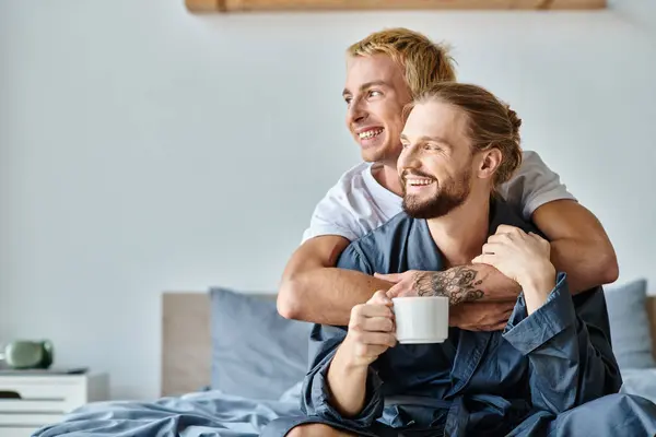 Joyful Tattooed Gay Man Embracing Bearded Boyfriend Coffee Cup Bedroom — Stock Photo, Image
