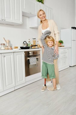 Mutlu anne engelli küçük kızın yanında duruyor protez bacaklarıyla fırın eldiveninde el sallıyor
