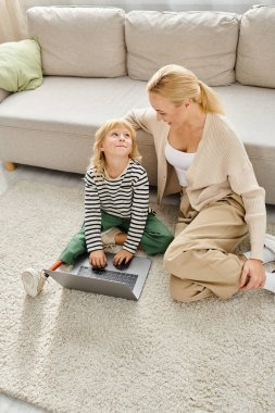 Protez bacaklı mutlu çocuk dizüstü bilgisayar kullanıyor ve annesiyle oturma odasında oturuyor.