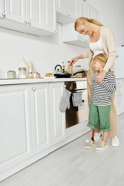 Mutfakta protez bacağı olan engelli bir kızın mutlu annesi yemek pişiriyor ve elini tutuyor.