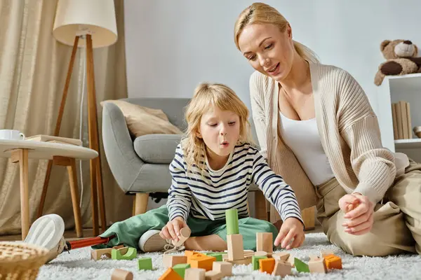 Heyecanlı, protez bacaklı küçük bir kız halının üzerinde oturuyor ve annesinin yanında tahta oyuncaklarla oynuyor.