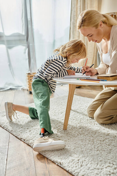 мать и ребенок с протезной ногой рисуют вместе на бумаге с красочными карандашами, качественное время