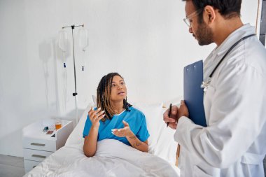 Çekici Afrikalı Amerikalı kadın hastane koğuşunda uzanmış Hintli genç doktoruyla konuşuyor.