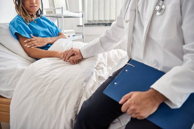 Genç Hintli doktor, Afro-Amerikan hasta elini tutarken hastane yatağında yatıyordu.