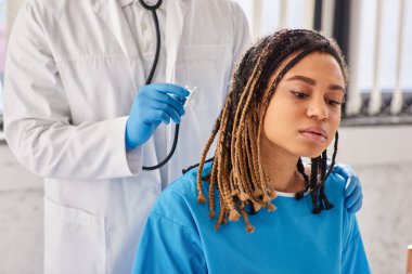 Hintli doktor, steteskop ve sağlık sigortası olan hasta Afrikalı Amerikalı hastasının nefesini dinliyor.