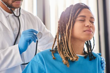 Hintli doktor, steteskop ve sağlık sigortası olan hasta Afrikalı Amerikalı hastasının nefesini dinliyor.
