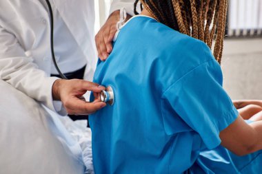 Genç Hintli doktor steteskop ve sağlık hizmeti kullanan Afrikalı Amerikalı hastasının nefesini inceliyor.
