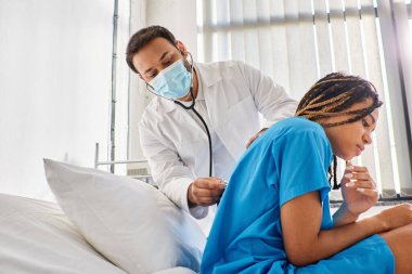 young indian doctor examining breath of ill african american patient with stethoscope, healthcare clipart