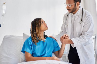 Ciddi Hintli doktor, Afrikalı Amerikalı üzgün hastasını hastane koğuşunda teselli ediyor.